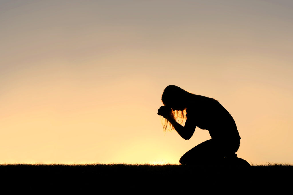 A young woman kneels in prayer outside at sunset asking the question, "Did Jesus meditate?"