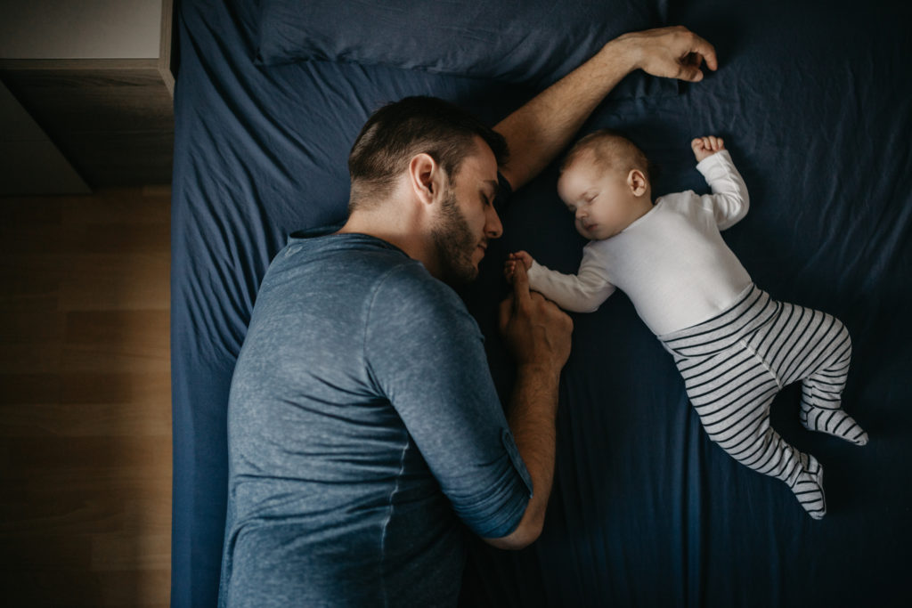 A man and his baby sleep soundly on a bed because they know that God's Word can help you sleep.