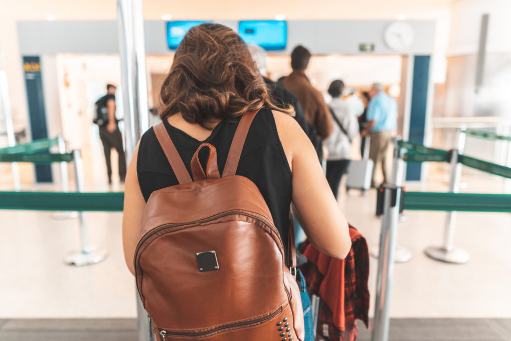 Woman with brown backpack goes through the security line at the airport, showing how staying calm when you travel is a good practice.