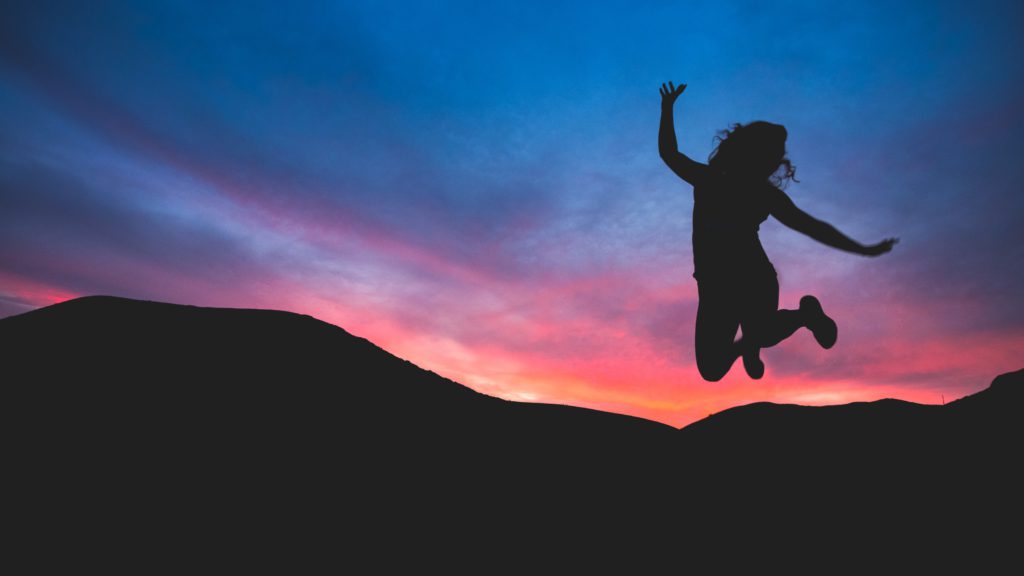 Woman in silhouette jumping in the mountains at dawn feeling joy over being alive in Christ.