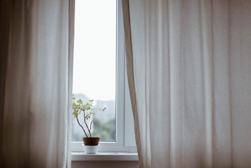 A plant in a white and brown pot sits on a windowsill surrounded by flowing white curtains showing that honoring God means doing what you were created to do.