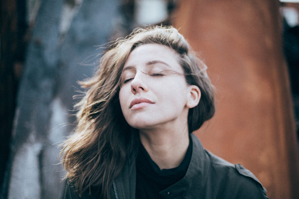 A young woman with long, light hair closes her eyes and breathes deeply to reduce stress.