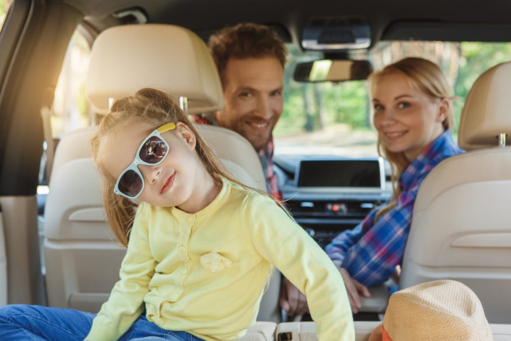 Young girl in blue sunglasses and yellow shirt awaits road trip fun with mom and dad this summer.