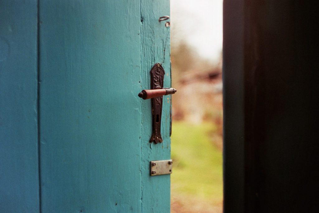 A teal door with a brass handle stands slightly ajar as you pray a prayer for new beginnings.