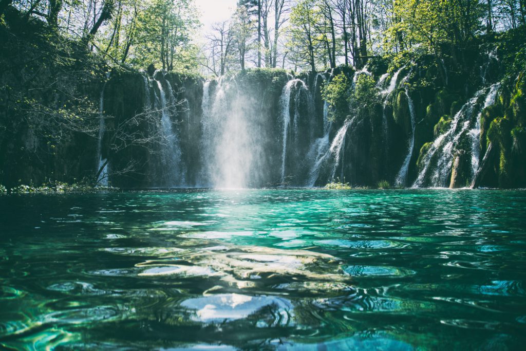 Water falls into a bluish green pond on a bright morning reminding us to pray a prayer for spiritual refreshment every day.