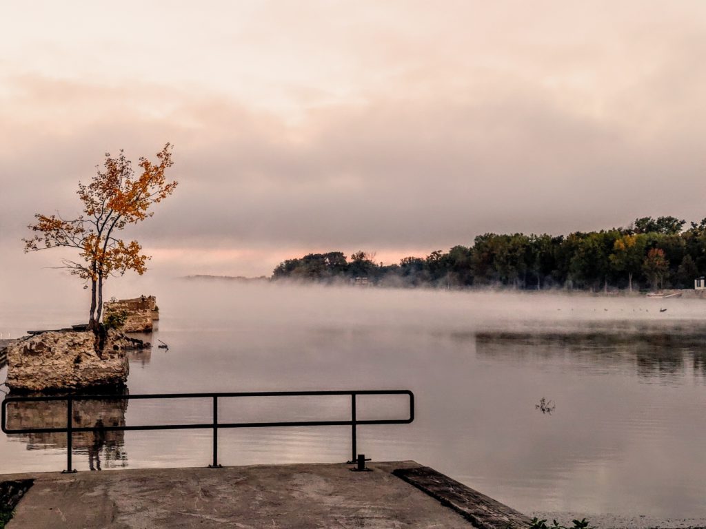 a lone tree with golden leaves stands on a rock in a latke with a dock in the foreground, providing a perfect place to pray a morning prayer for rest.