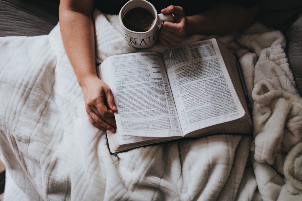 A person sits with an open Bible and a cup of coffee on a white blanket praying a morning prayer about loving God.