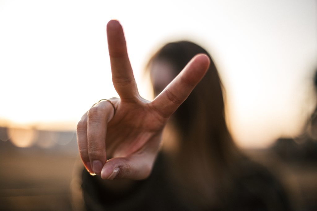 A woman blurred in the background holds her fingers in the shape of the letter V as she remembers a morning prayer for victory over sin.