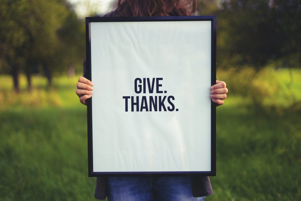 A person holding a sign with the words "give thanks" on it reminds us to pray a morning prayer of thankfulness every day.