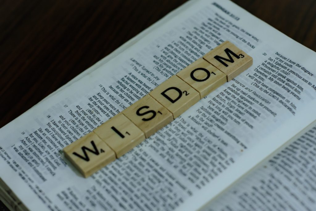 The word "wisdom" in Scrabble letters lies on a page of an open Bible reminding us to pray a morning prayer for wisdom and rest in God's Word.