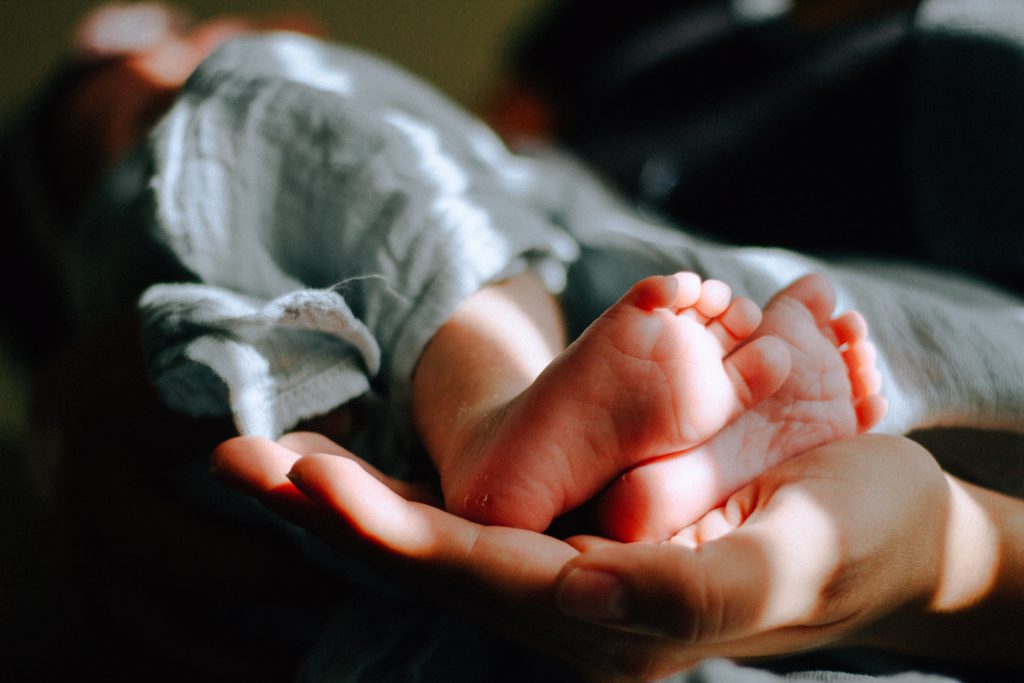 A parent's hand cradling bare baby's feet remind us to pray a one-minute prayer for a new baby.