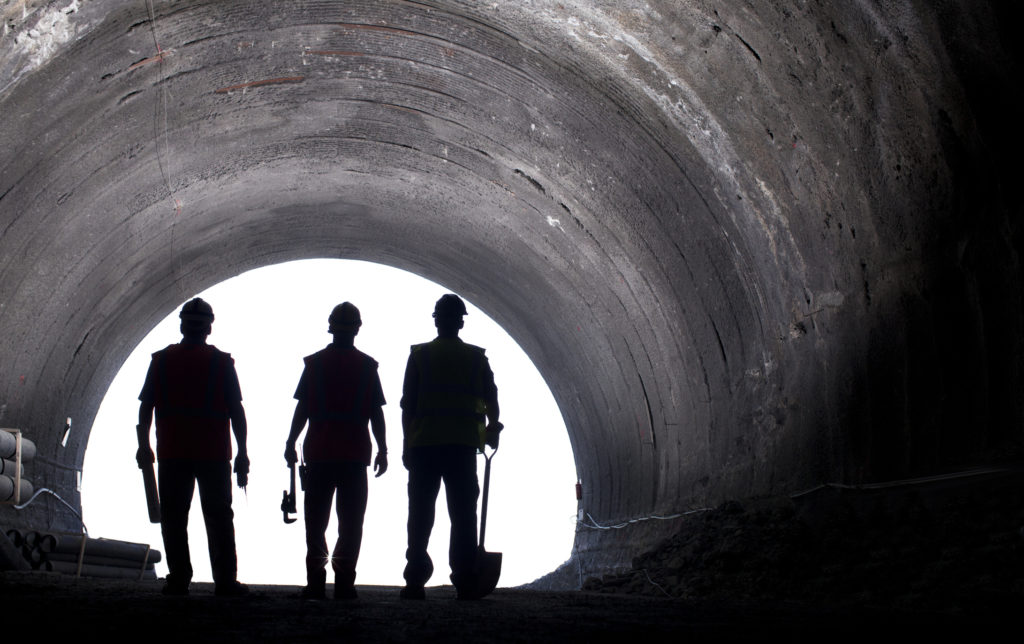 Three workers stand silhouetted in a tunnel, reminding us to pray a prayer for laborers this Labor Day.