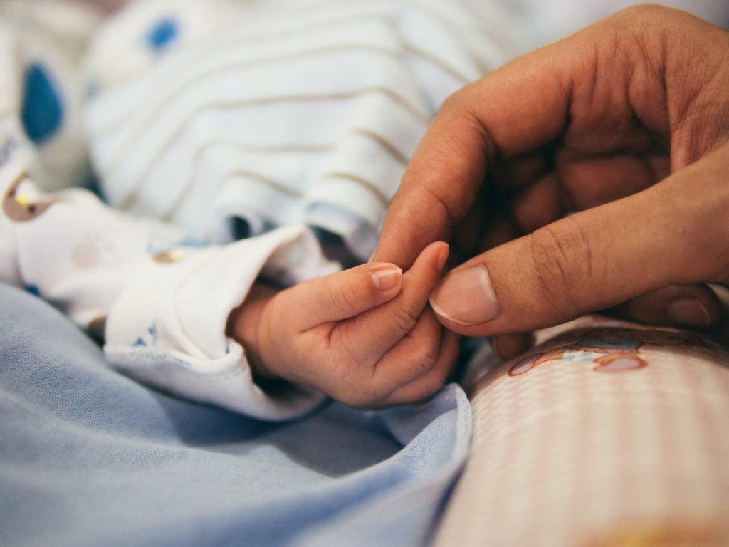 A mom holds the hand of her small child lying in bed as she prays a prayer for kids facing cancer.