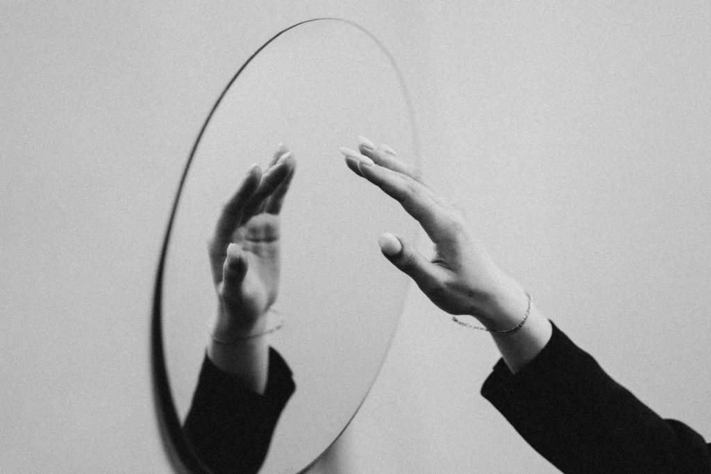 A woman's hand in black and white reaches toward a mirror, remind us to pray a prayer for transformation.