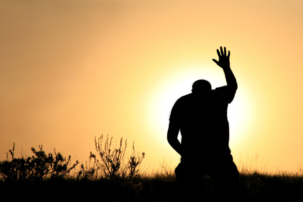 A silhouetted man raises a hand in prayer at sunset as he prays a prayer when you're disappionted.