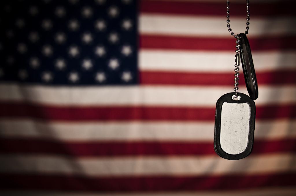 Dog tags hand in front of an American flag reminding us to say a prayer for veterans.