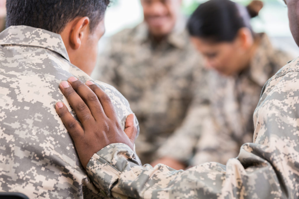 One soldier places his hand on the shoulder of another shoulder as they pray a prayer for veterans.