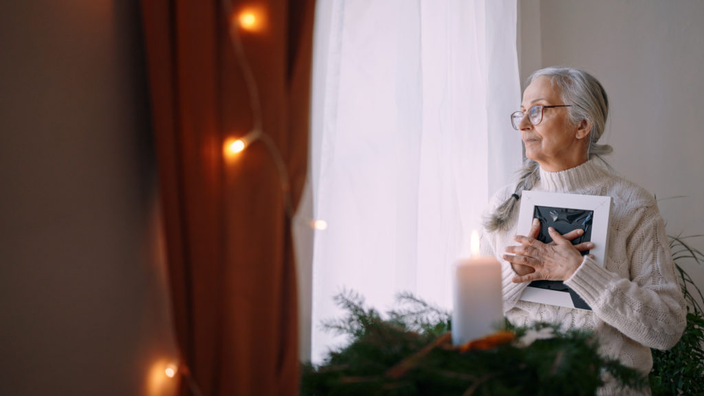 An elderly woman holds a frame to her heart at Christmastime as she prays a prayer for those who grieve.