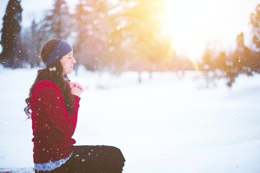 A woman in a red sweater outside in the snow prays a prayer for the new year.