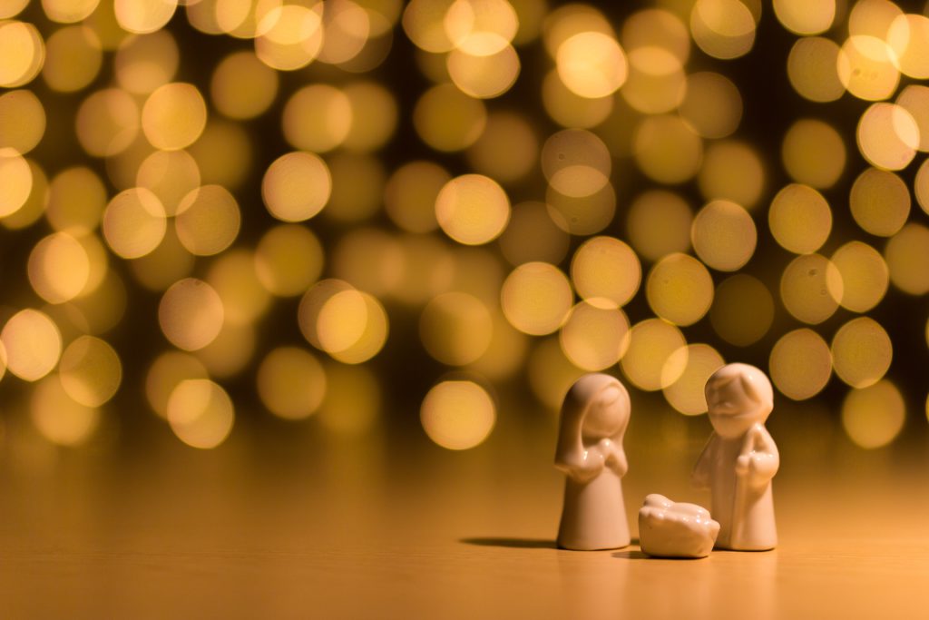 An alabaster Holy family offers a Christmas prayer in front of sparkling amber lights.