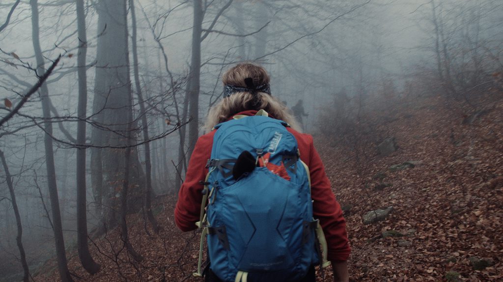 A woman with a blue backpack walks through a misty wood knowing that having courage helps you to stop worrying.