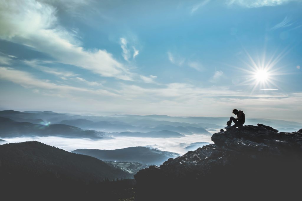 A man sits on a mountaintop  in the late afternoon learning how to encourage your faith.