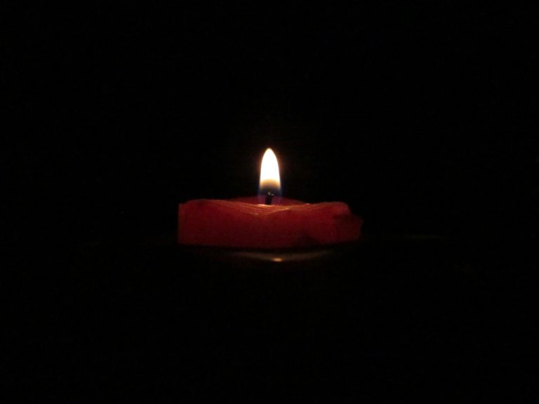 A lit candle in the darkness illustrates finding joy in our trials.