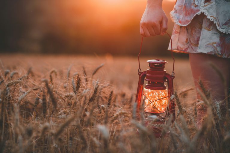 A woman holding a lit lantern in a field at sunset reminds us to let our light shine as we live like Jesus.