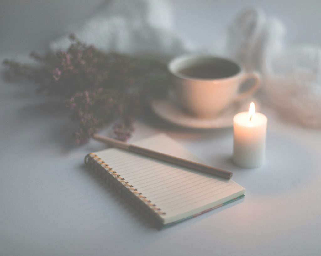 A warm cup of tea, a lit candle and a notebook stand ready to contain what you're thankful for as you practice Christian meditation for restful sleep.
