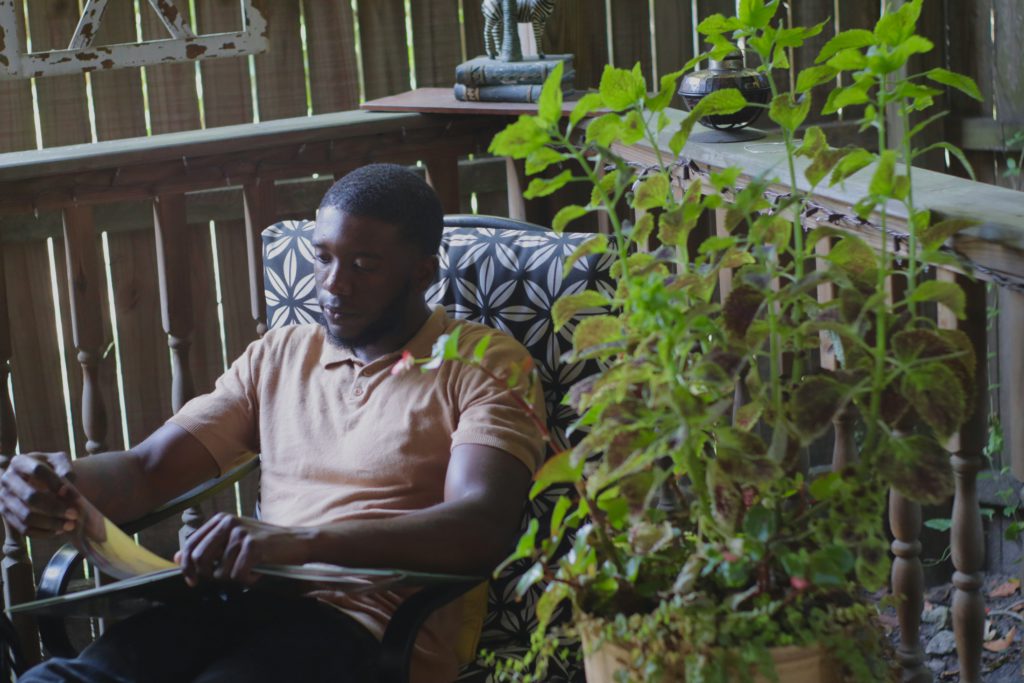 An Black man sits in a chair on his deck near a large leafy plant learning biblical truths about rest.