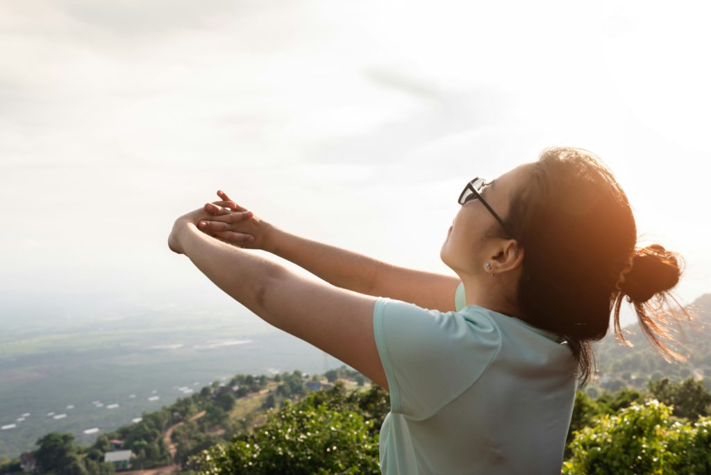 A young Asian woman practices breathing exercises on a mountain.