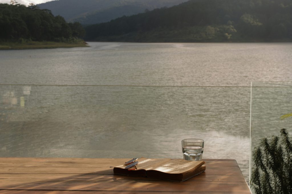 An open Bible and a glass of water on a table overlooking a lake are part of building healthy habits.