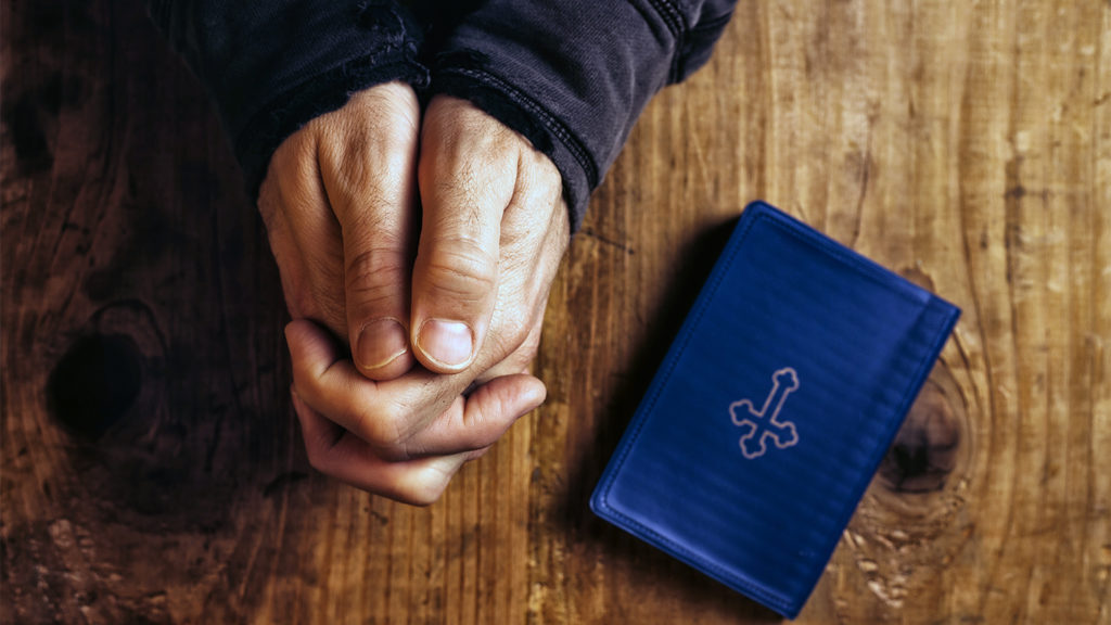 Royalty Free Stock Photo: A man's hands clasped in nighttime prayer, with a Bible resting nearby