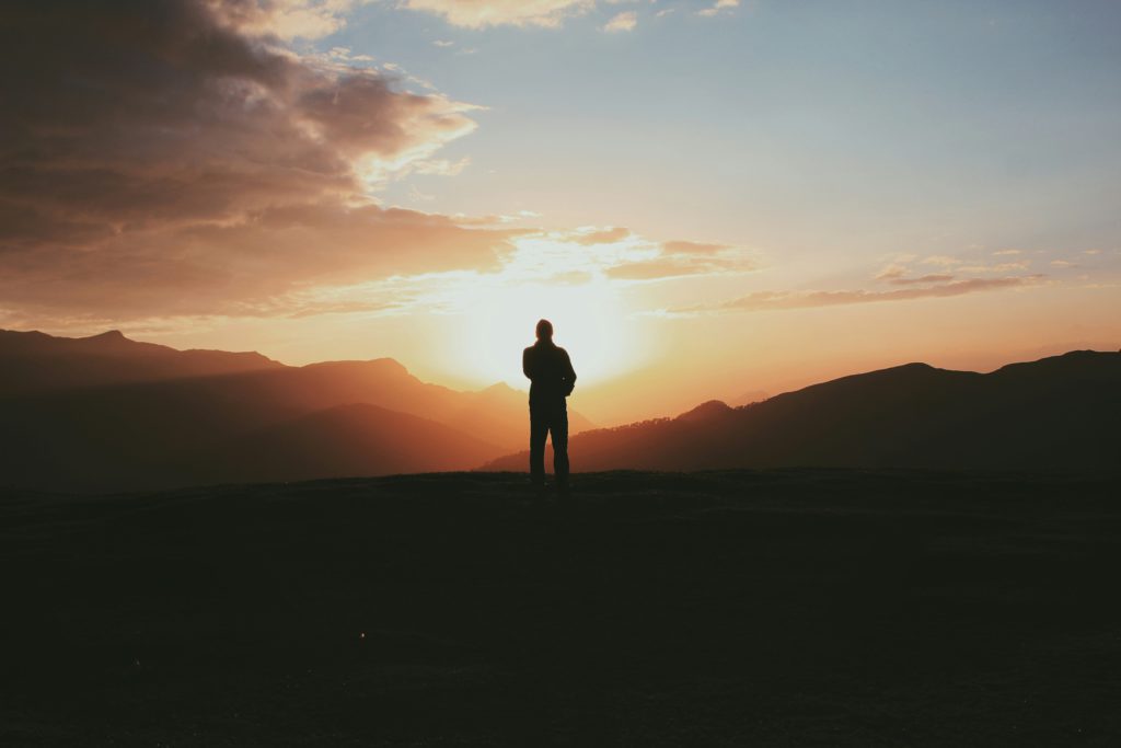 A man at sundet on a mountain praying alone.