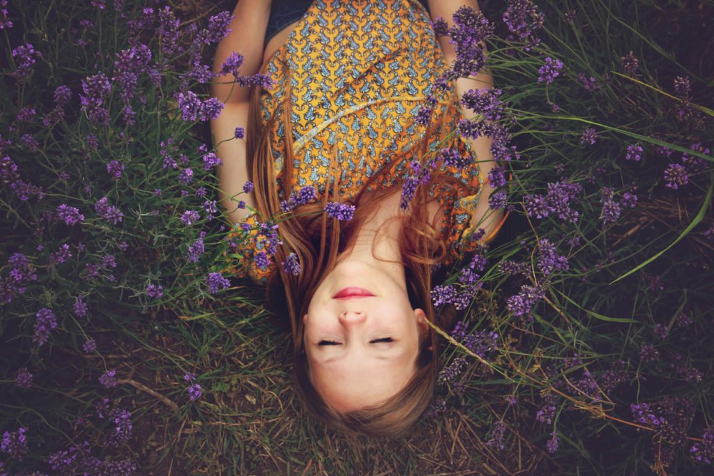 A young woman in a field of lavender smiles as she anticipates a restful night of sleep.
