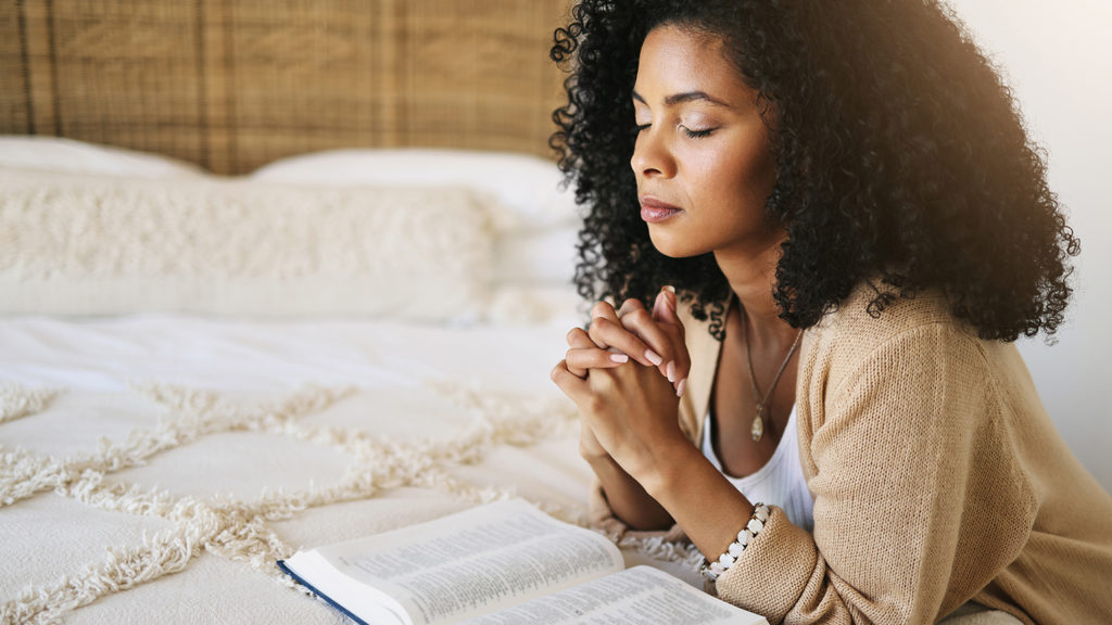 Royalty-free stock photo: A woman prays over an open Bible at her bedside
