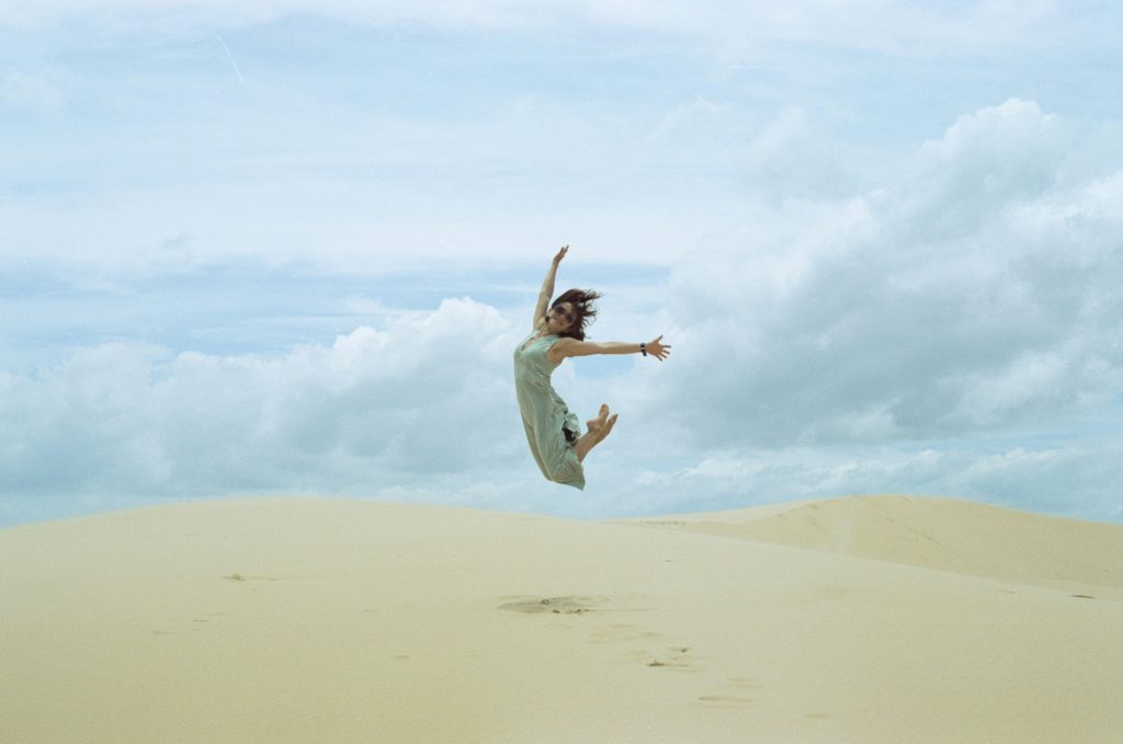 A young woman in a cool dress leaps on the sand after letting go of her will.