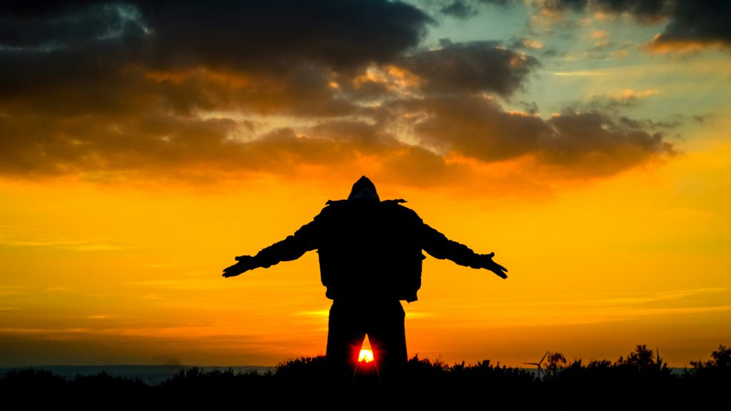 A man stands in silhouette facing a brilliant sunset as God is exalted in his heart.