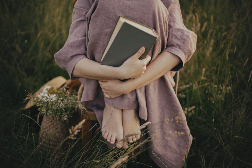 A young girl in a rose-pink dress sits in a field of grasses holding a Bible seeking the connection between truth and faith.