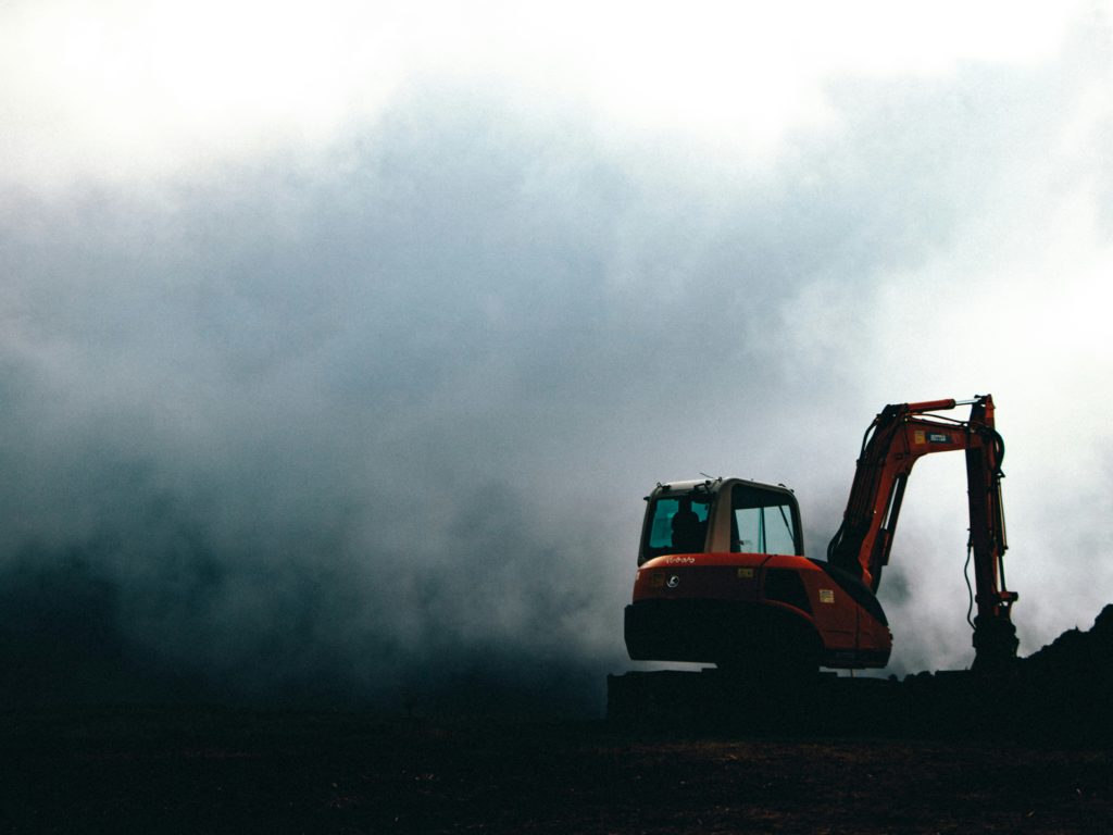 A red excavator waits in the fog for deconstruction to begin.