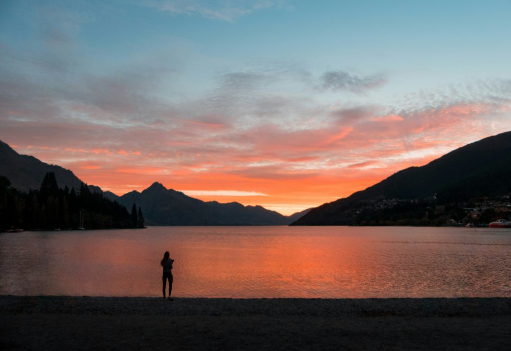 A woman stands in silhouette beside a mountain lake at sunset letting nature help her move from fear to awe of God.