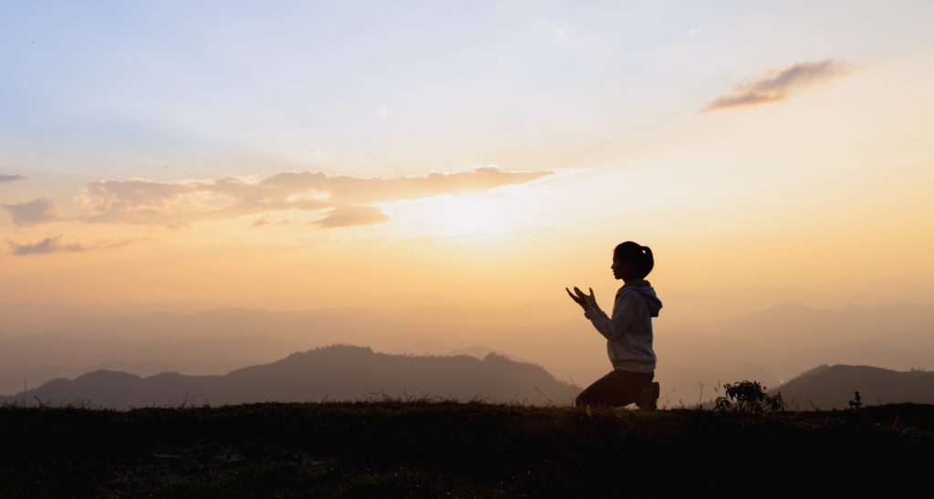 Silhouette of a woman praying outside at beautiful landscape at the top of the mountain as she learns to let go of her own plans.