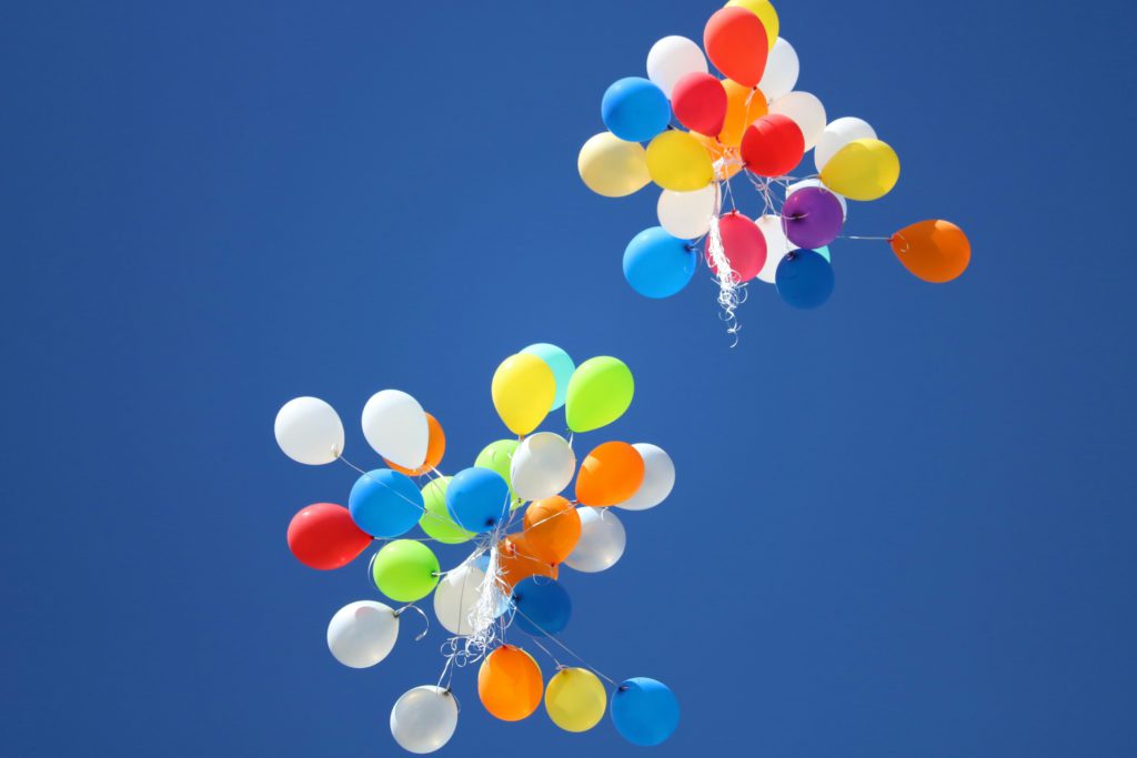 2 large bunches of colorful balloons float in a bright blue sky as they're released in an act of surrendering.