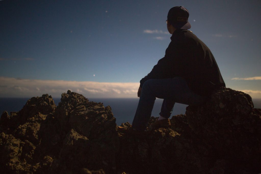 A man sits on a rock in the mountains rekindling his faith by overcoming skepticism.