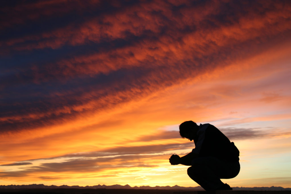 A man in silhouette prays during a blazing sunset as he learns the importance of surrender and submission.