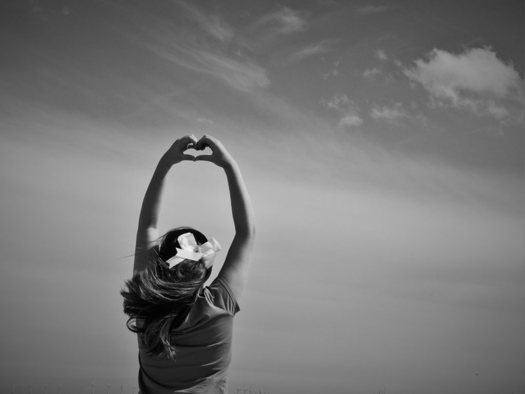 In a black and white photo, a woman holds her hands up to the sky in a heart shape showing how she is surrendering her heart to God.