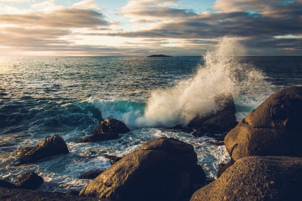 Waves crashing against rocks at sunrise remind us to keep trusting in God's power.