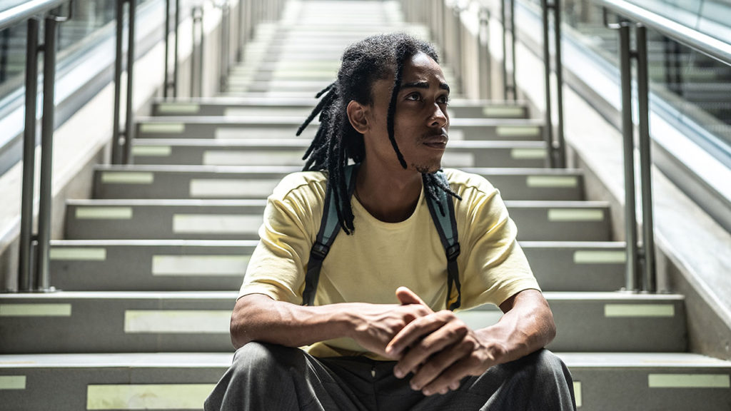 Contemplative young Black man sitting on the stairs in the subway station thinking about the enemy of contentment.