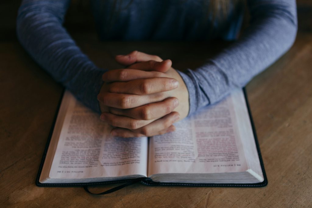 Folded hands on an open Bible show how you can learn what God can do.