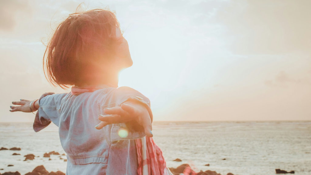 A young woman stretches her arms out wide on the shore as she discovers her God-given value.